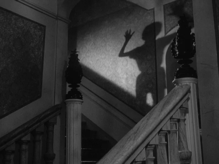 The Silence (1963) movie still: wide — A grand staircase features patterned wallpaper and decorative finials atop the newel posts. An oversized,…