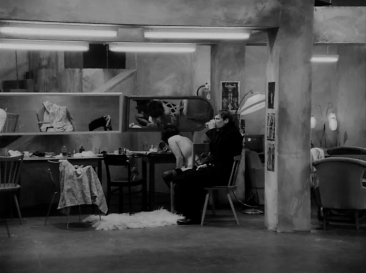From the Life of the Marionettes (1980) movie still: wide — A utilitarian dressing room features minimalist furniture, bare walls, and multiple…