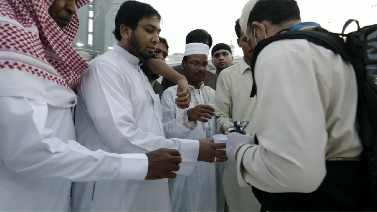 One Day in the Haram (2017) movie still: medium — An outdoor courtyard area with several men in traditional clothing gathering together. A person…