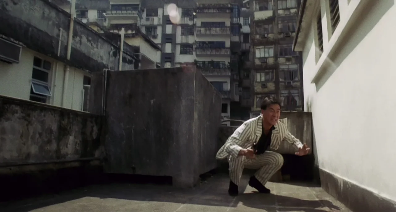 The Killer (1989) movie still: fullbody — An urban rooftop with gray concrete structures and high-rise residential buildings in the background. A…