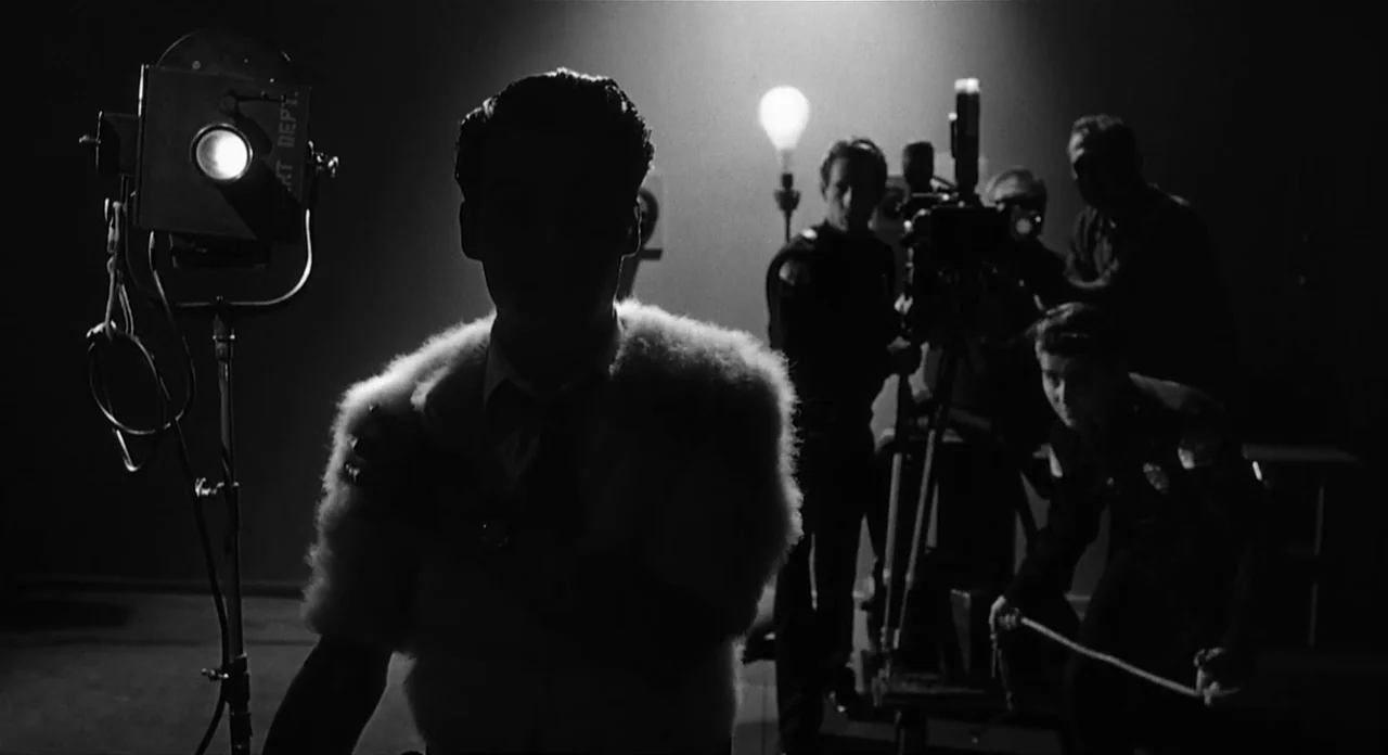 Ed Wood (1994) movie still: medium — A dark film set with professional recording equipment and a single overhead bulb. A man in a fur coat faces the…