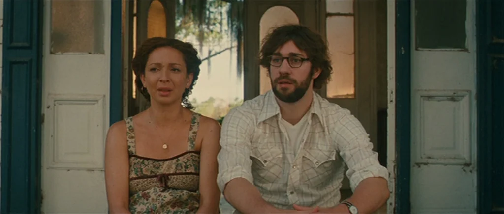 Away We Go (2009) movie still: medium — A wooden porch entrance with white double doors featuring paneled wood details. A woman and man sit side by…