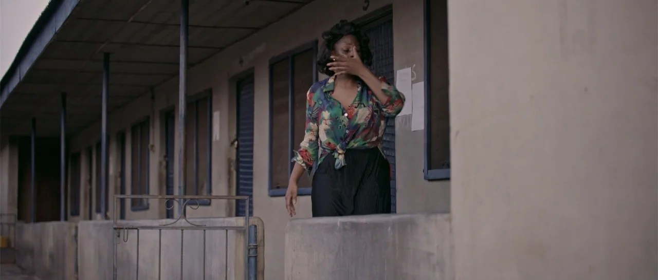 Crossroads (1986) movie still: medium — An exterior corridor of a plain motel features weathered walls and dark window frames. A woman in a floral…