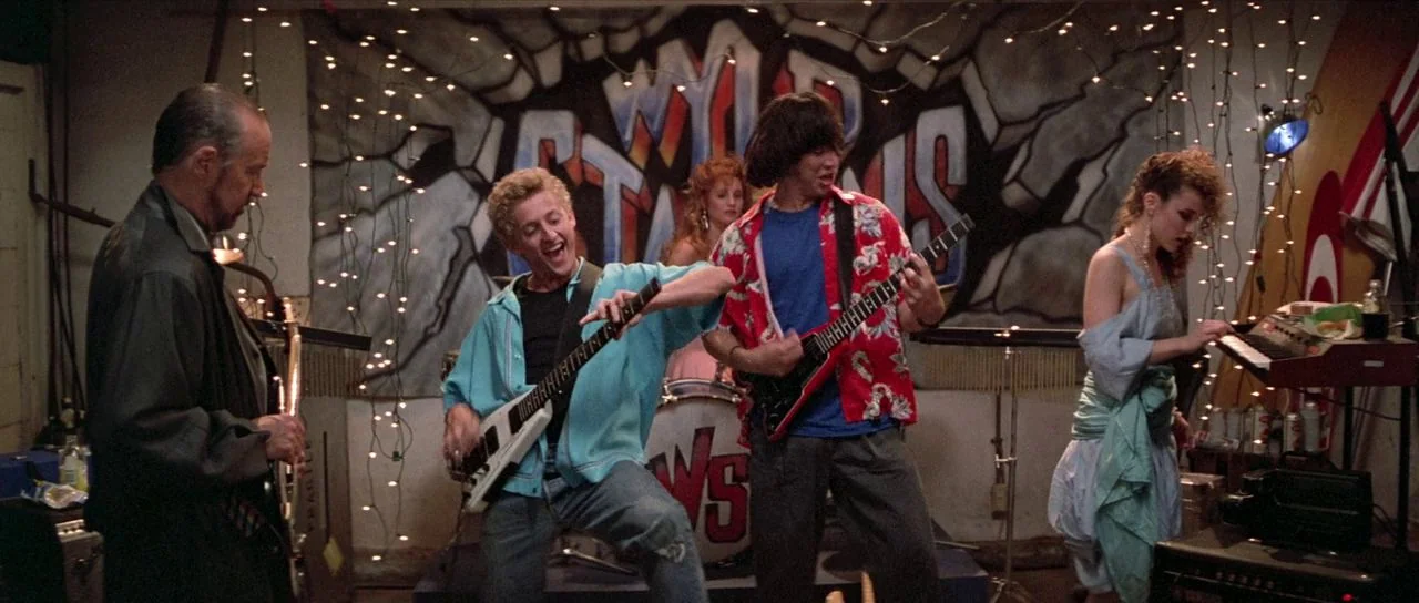 Bill and Ted’s Excellent Adventure (1989) movie still: medium — A cluttered suburban space transformed into a rehearsal area with graffiti on the…