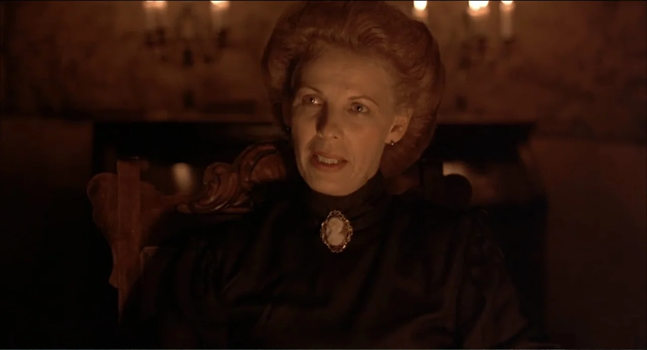 Like Water for Chocolate (1992) movie still: medium — A dark, dimly lit 19th-century interior with faint background wall patterns. An older woman in…