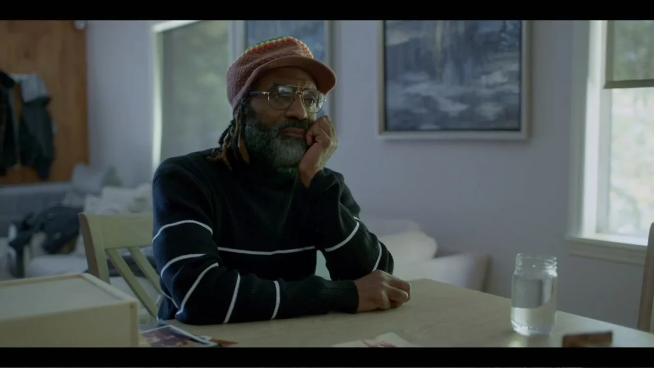 Diddy: The Making of a Bad Boy (2025) movie still: medium — A quiet dining room with soft light and a framed picture on the wall. A man with a beard…