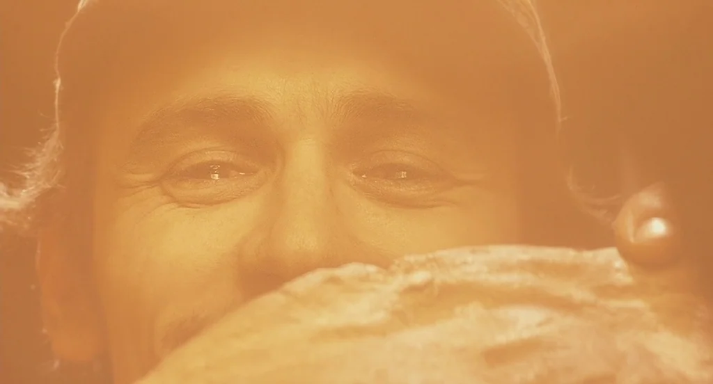 127 Hours (2010) movie still: closeup — A close-up of a person's face bathed in an intense golden light. The subject holds a rough, textured,…
