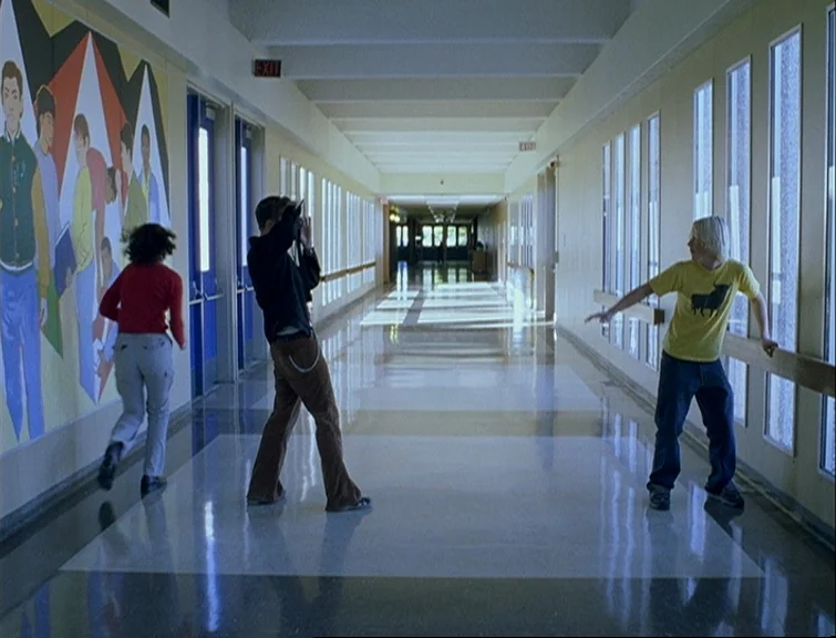 Elephant (2003) movie still: fullbody — A long, brightly lit school corridor features a large, colorful abstract wall mural. Three teenagers…