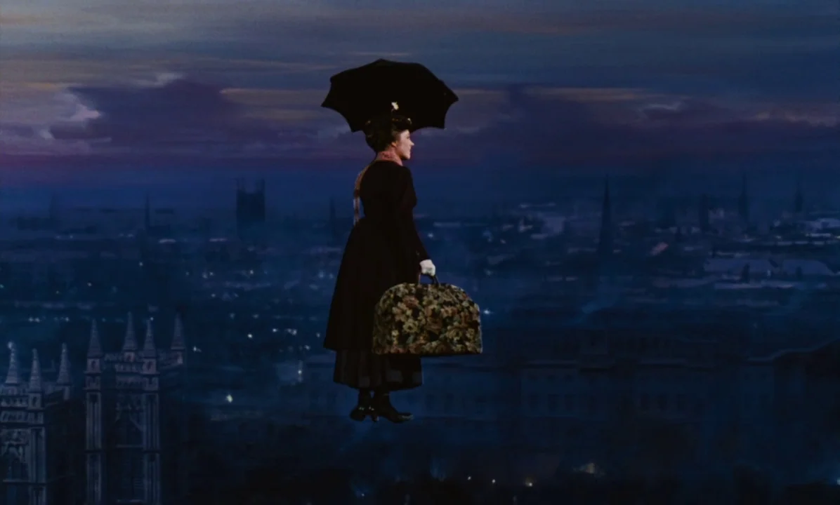 Mary Poppins (1964) movie still: wide — A woman drifts through the air over a sprawling, dark, silhouetted European-style cityscape at night. She…