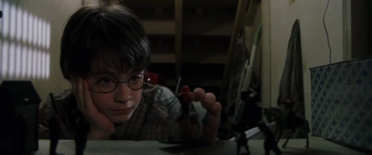 Harry Potter and the Philosopher's Stone (2001) movie still: medium — A dark, cramped space under stairs with wooden rafters and sparse, cluttered…