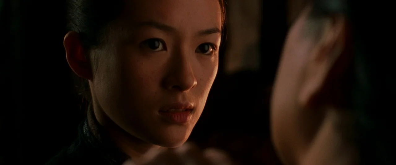 Crouching Tiger, Hidden Dragon (2000) movie still: closeup — A woman stares intently at an obscured person in a dark, dimly lit room. She holds a…