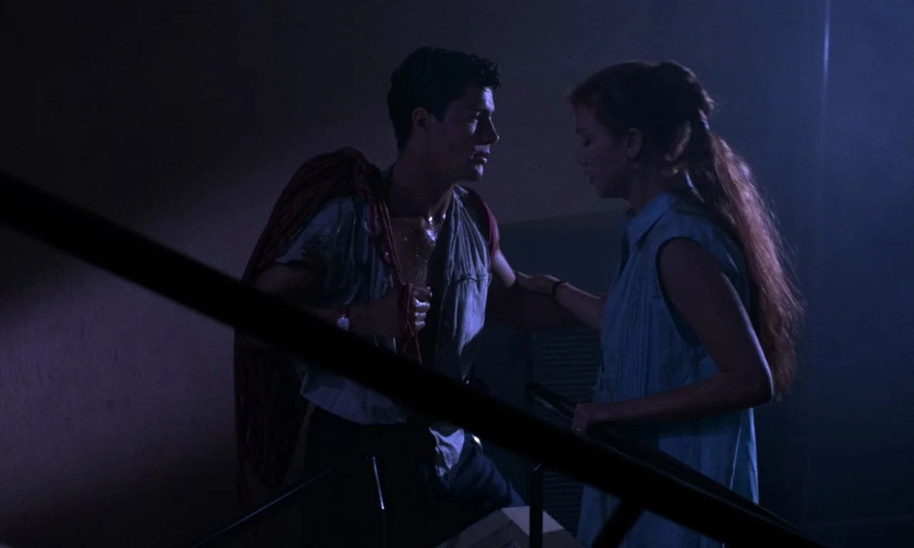 Demons 2 (1986) movie still: medium — A dimly lit indoor stairwell with metal handrails visible in the foreground. A man and a woman stand close to…