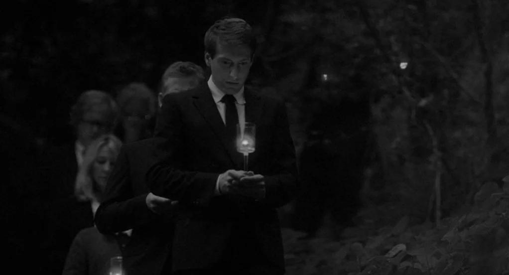 Much Ado About Nothing (2012) movie still: medium — A group of people walks along a darkened wooded path at night. A young man in a suit leads the…