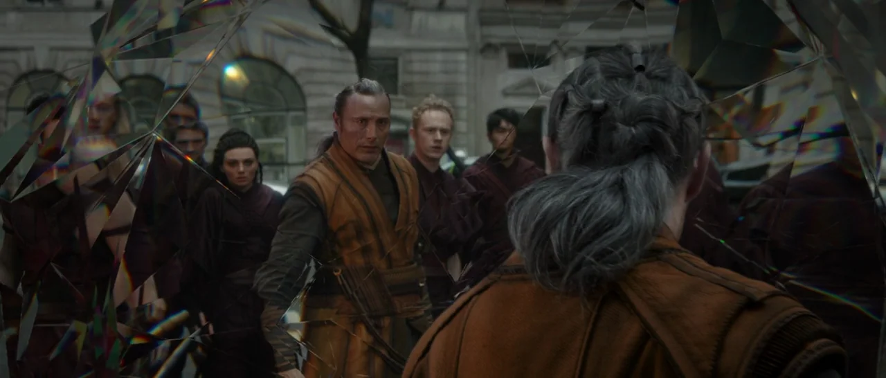 Doctor Strange (2016) movie still: medium — A group of people wearing matching orange tunics stand on a city street. The scene is viewed through a…