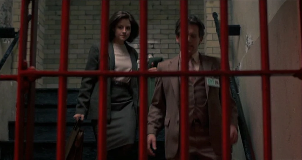 The Silence Of The Lambs (1991) movie still: medium — A dimly lit stairwell features white brick walls and a stark red metal grate. A young woman…