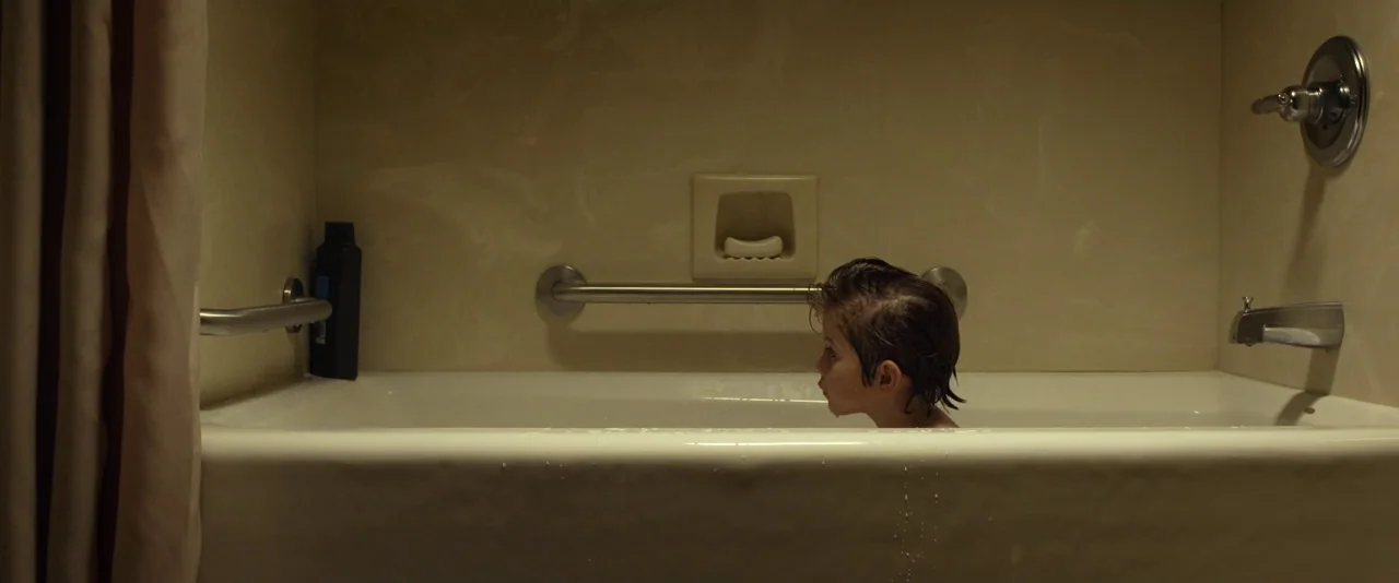 Before I Wake (2016) movie still: medium — A porcelain bathtub with metal grab bars and a black bottle stands against tile. A young child with damp…