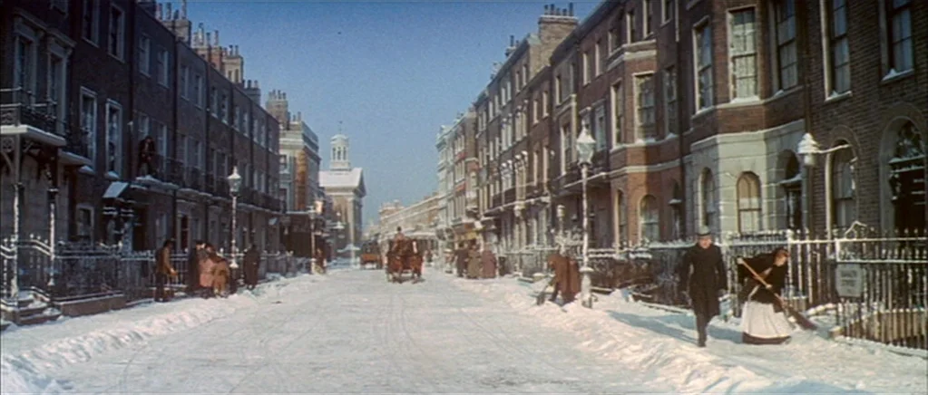 The Private Life of Sherlock Holmes movie still: wide — A snow-covered Victorian street is lined with multi-story brick residential townhouses.…