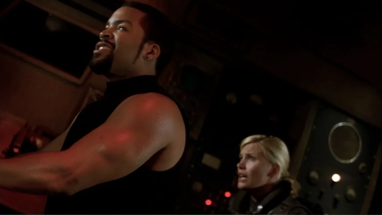Ghosts of Mars (2001) movie still: medium — A dimly lit technical control room features large equipment panels with various gauges. A man and a…