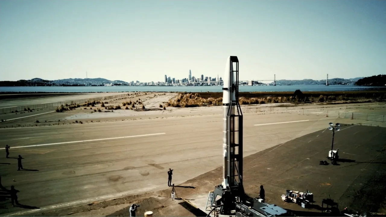 Wild Wild Space (2024) movie still: wide — A wide abandoned runway stretches toward a distant bay with a city skyline backdrop. Several individuals…