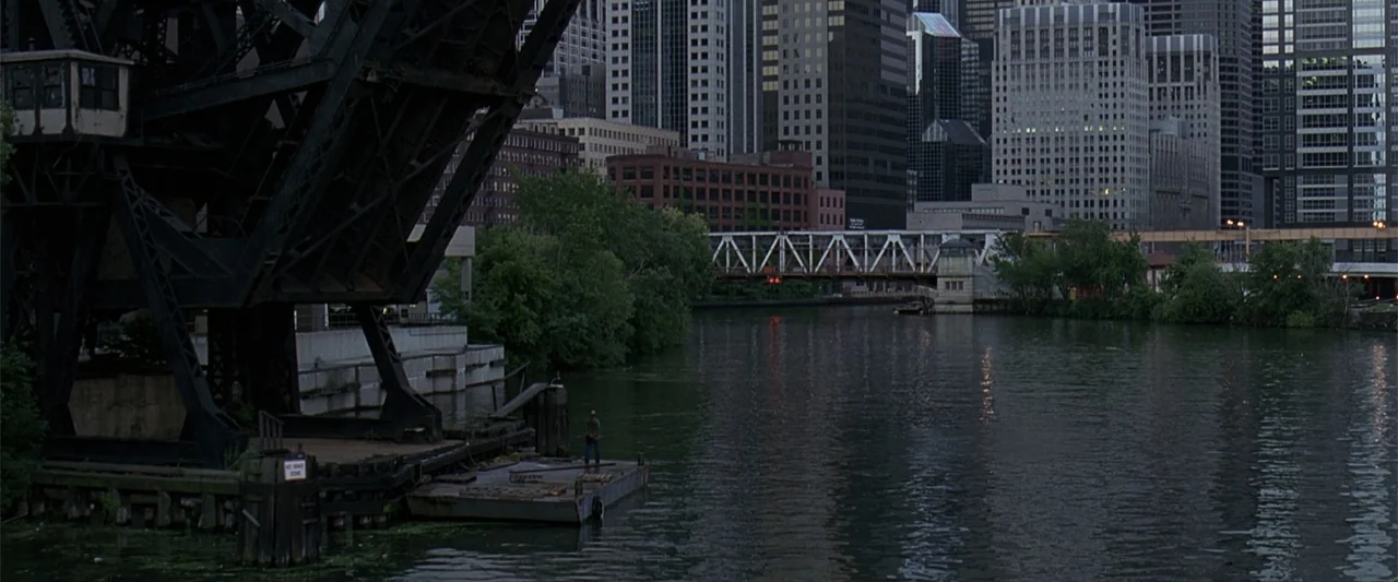 A Family Thing (1996) movie still: wide — A city skyline rises behind a river with a large bridge structure. A lone person stands on a small…
