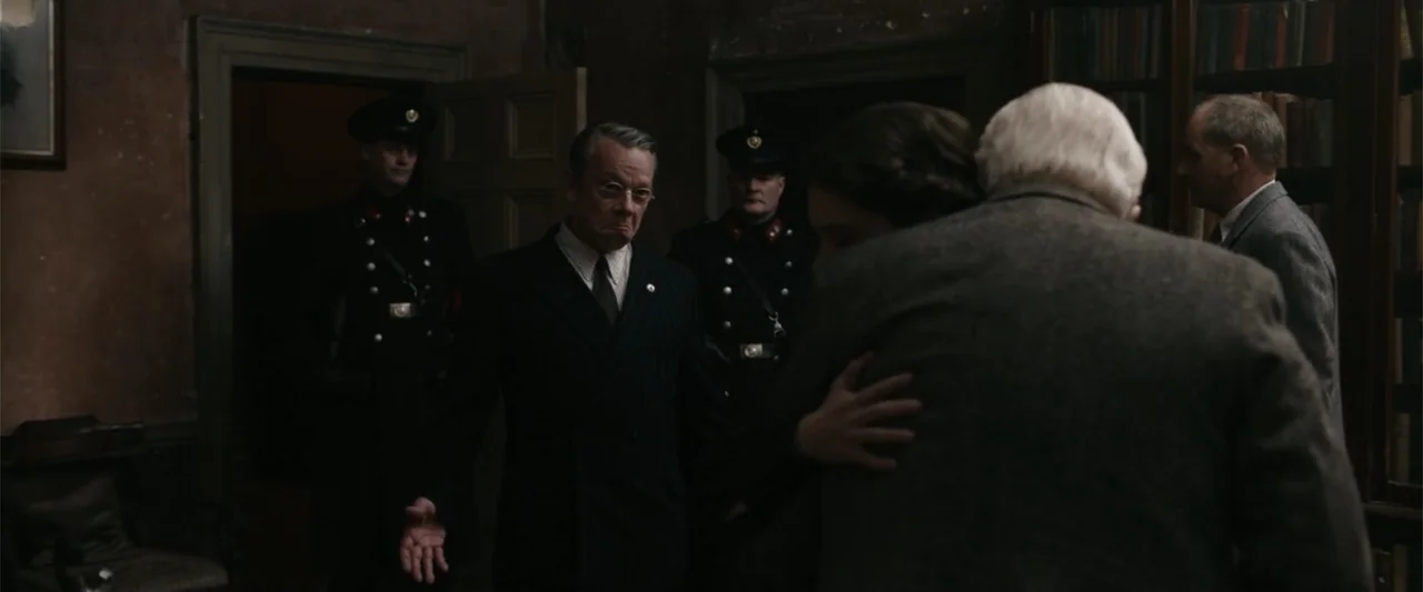Freud's Last Session (2023) movie still: medium — A dark, wood-paneled study or library with shelves of books lining the walls. A middle-aged man in…
