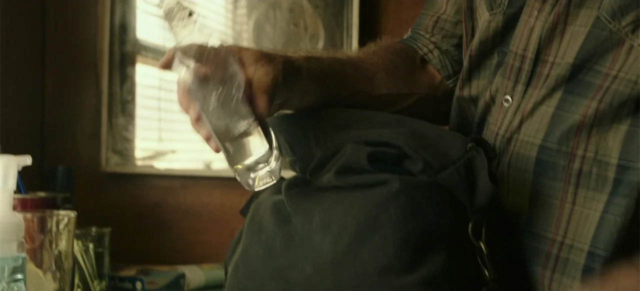 Blood Father (2016) movie still: medium — An interior space with wood-paneled walls and a window featuring horizontal blinds. A person holds a clear…