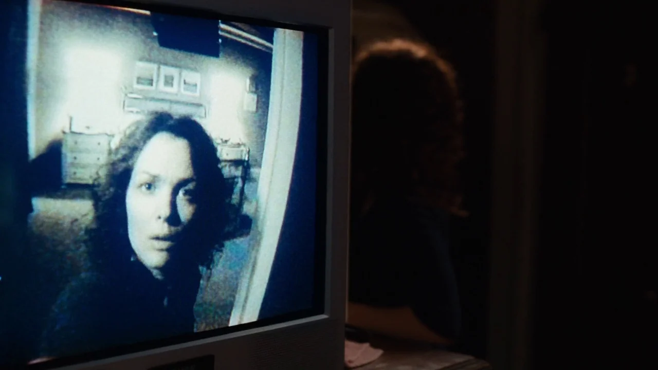 Saw III (2006) movie still: medium — A dark living room holds a CRT television displaying a live-feed video surveillance shot. A woman with dark…