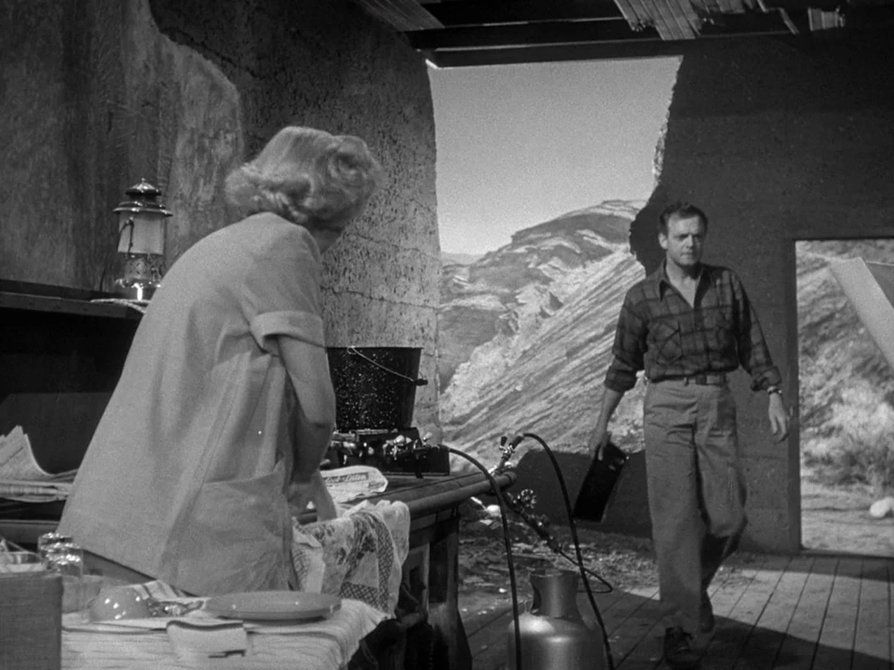 The Prowler (1951) movie still: medium — An open stone structure overlooks a rugged desert mountain landscape. A man walks toward a woman working at…