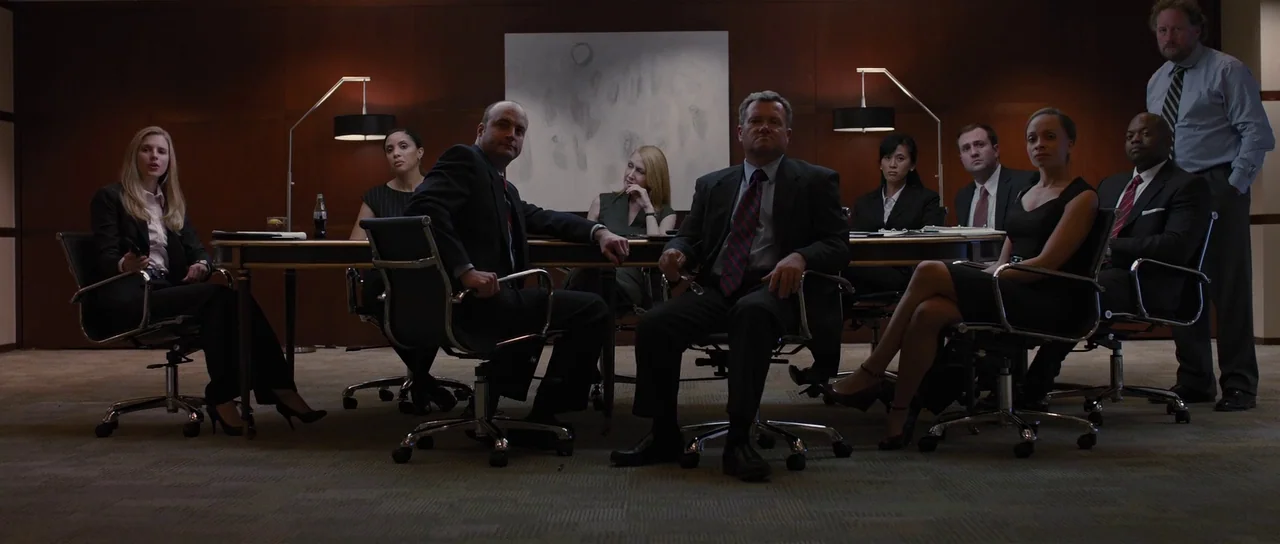 The East (2013) movie still: wide — A dark, wood-paneled corporate meeting room features a large rectangular table and ergonomic chairs. A group of…