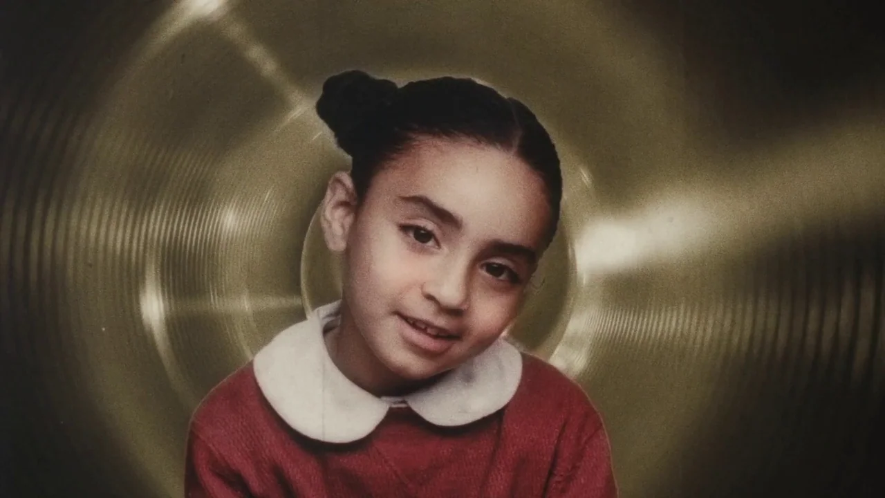 Once Within A Time (2022) movie still: closeup — A young girl with high buns stands against a stylized, circular metallic background. The child…