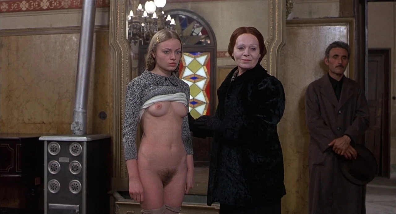 Salò, or the 120 Days of Sodom (1975) movie still: A quiet, tense inspection takes place in a dimly lit, dated room. The composition emphasizes the…