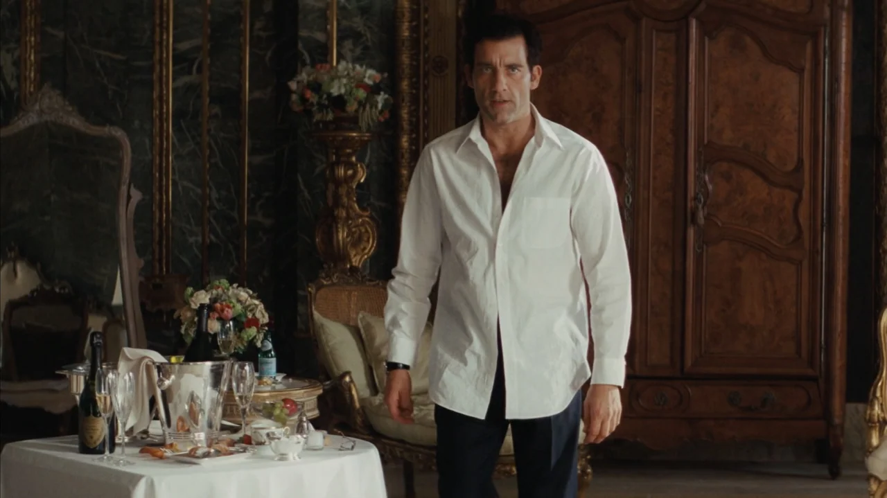 Duplicity (2009) movie still: fullbody — An opulent hotel suite features dark marble walls and an ornate wooden wardrobe. A man wearing an…