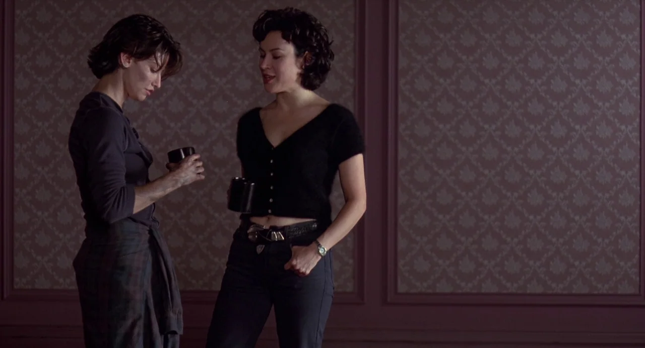 Bound (1996) movie still: medium — A dimly lit room features walls covered in dark-toned, intricate floral pattern wallpaper. Two young women stand…