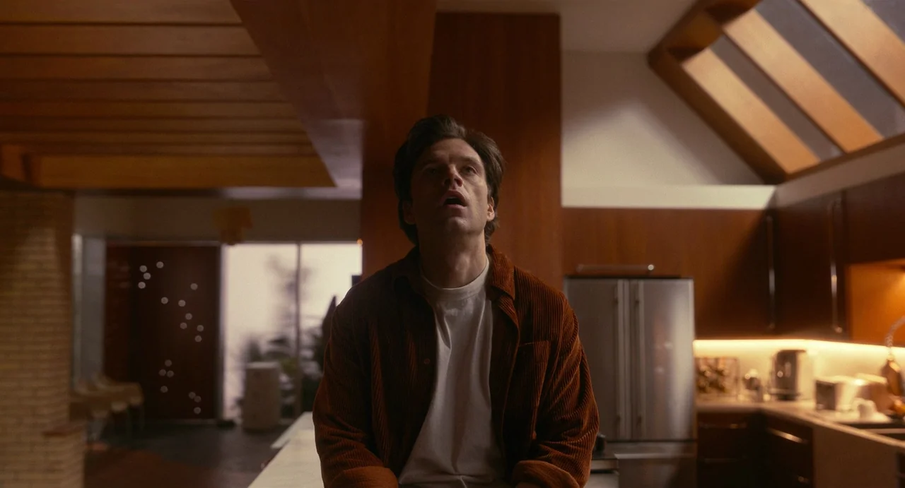 Fresh (2022) movie still: medium — A modern kitchen features rich wood cabinetry and an angled skylight overhead. A man sits on the counter while…