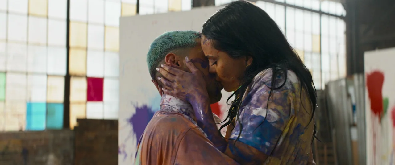 Do Revenge (2022) movie still: medium — A spacious art studio with large multi-paned industrial windows and blank canvases in background. A couple…