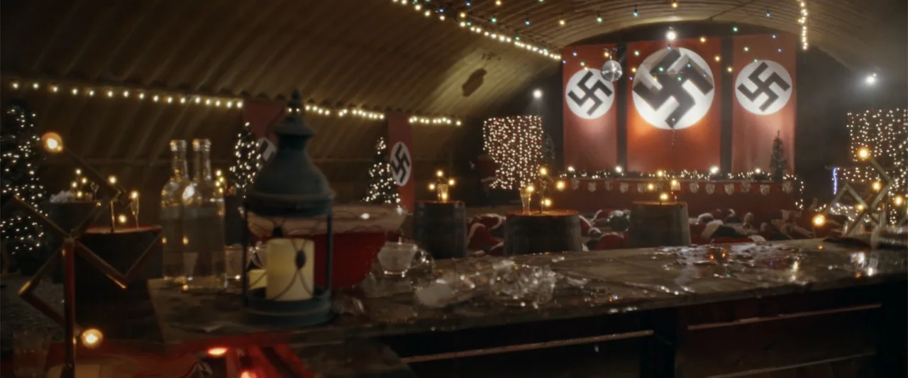 Silent Night, Deadly Night (2025) movie still: wide — A curved military bunker interior decorated with holiday lights and swastika banners on walls.…