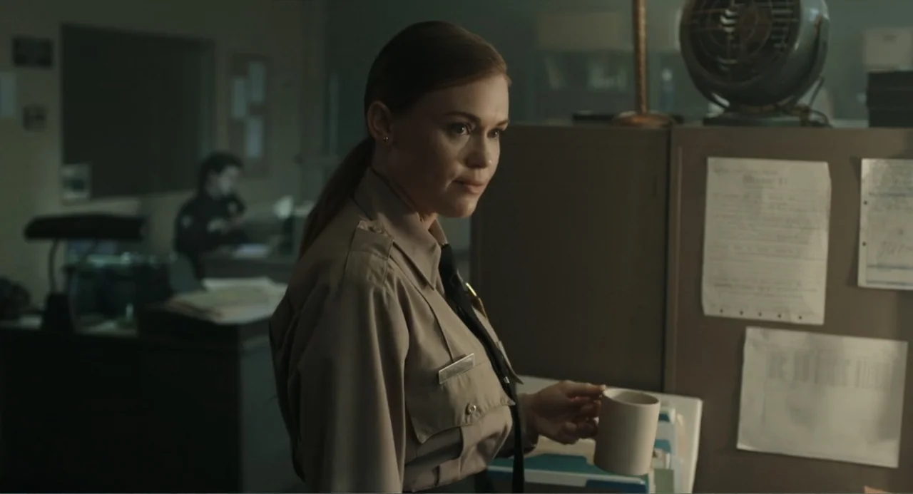 Ted Bundy: American Boogeyman (2021) movie still: medium — A dimly lit police station office contains gray filing cabinets and documents pinned to…
