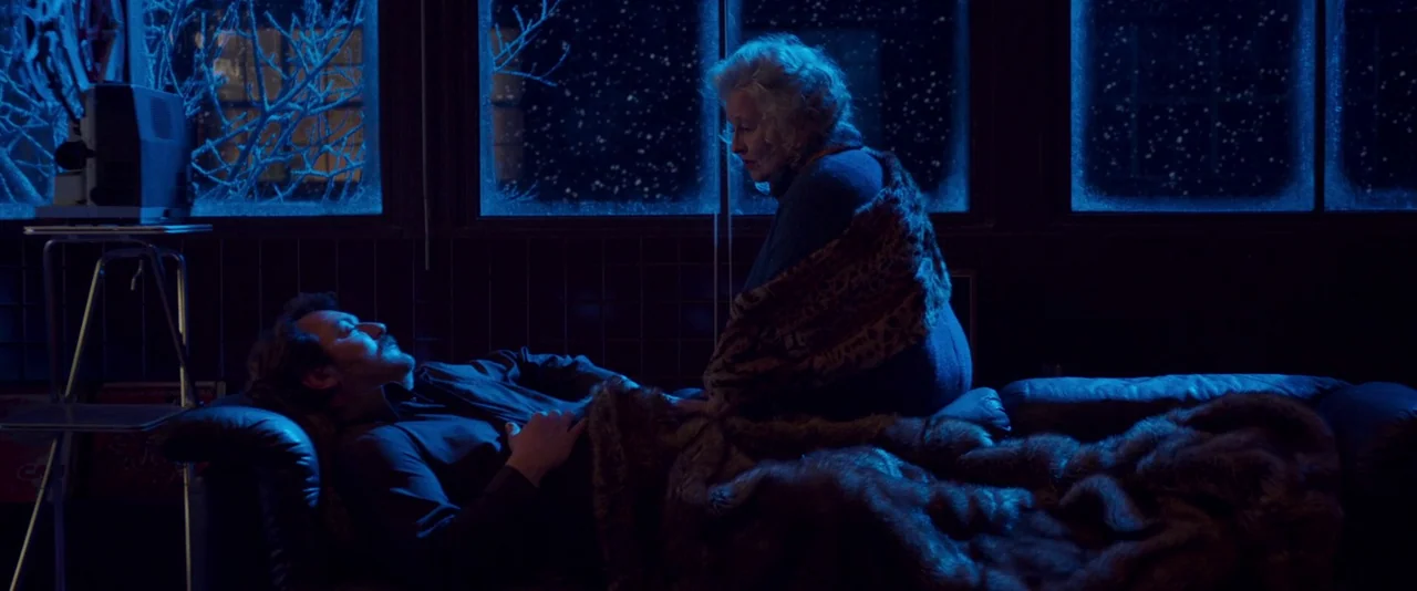 Peter Von Kant (2022) movie still: medium — A darkened interior room with large windows showing snow falling against the dark night sky. An elderly…