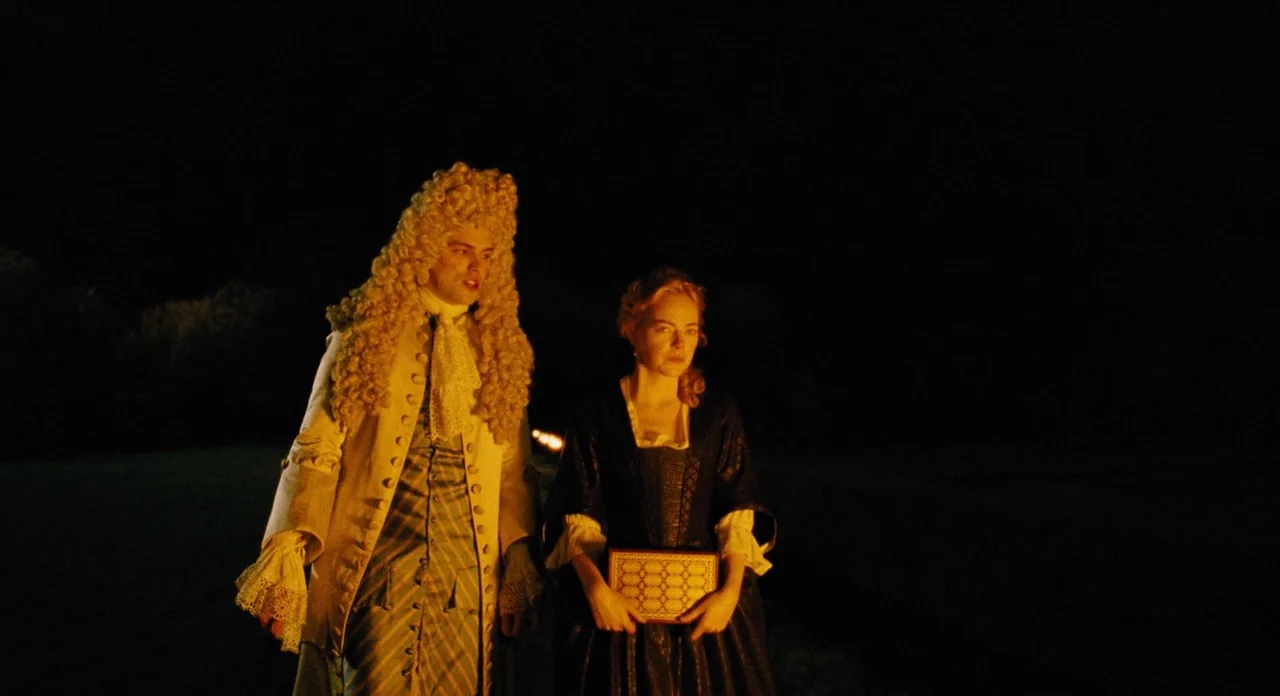 The Favourite (2018) movie still: medium — A dark, open field at night is lit by a low-level warm glow. A man and woman in historical attire walk…