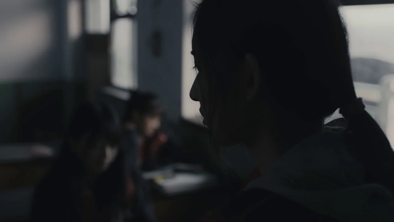 An Elephant Sitting Still (2018) movie still: closeup — A dimly lit classroom features windows providing soft light against the silhouetted subject.…