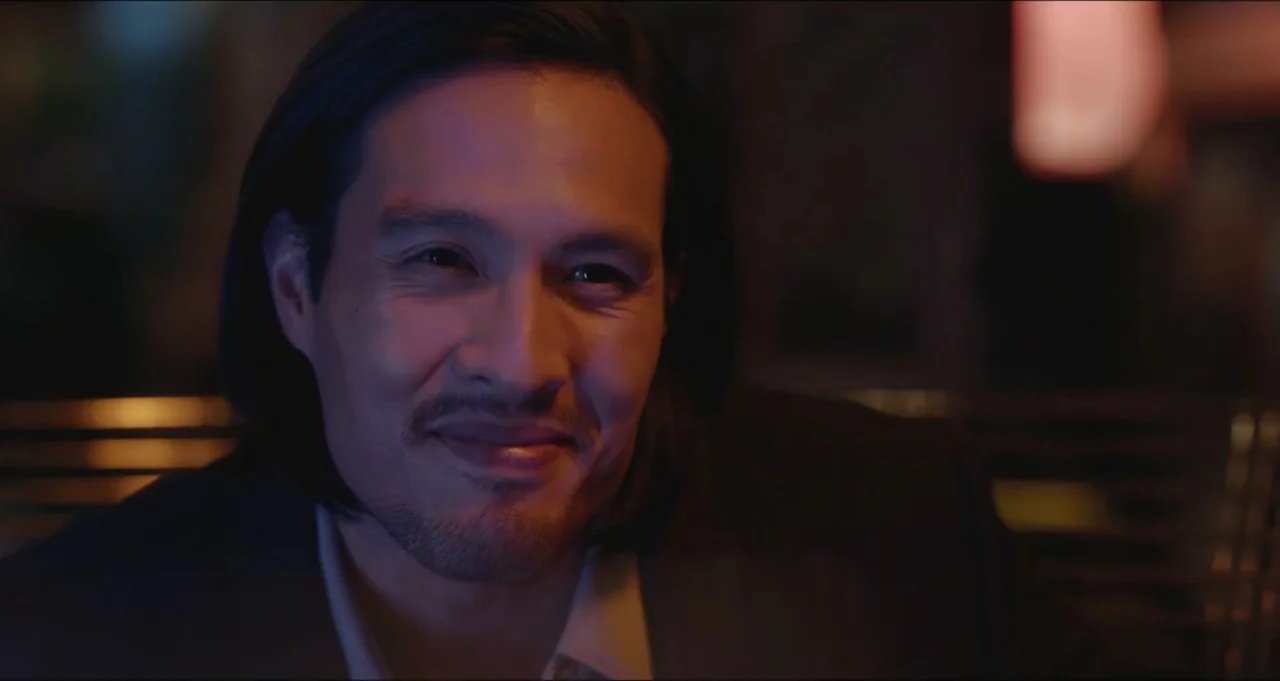 Five Blind Dates (2024) movie still: closeup — A dimly lit lounge setting provides the backdrop for a close portrait. A middle-aged man with dark…