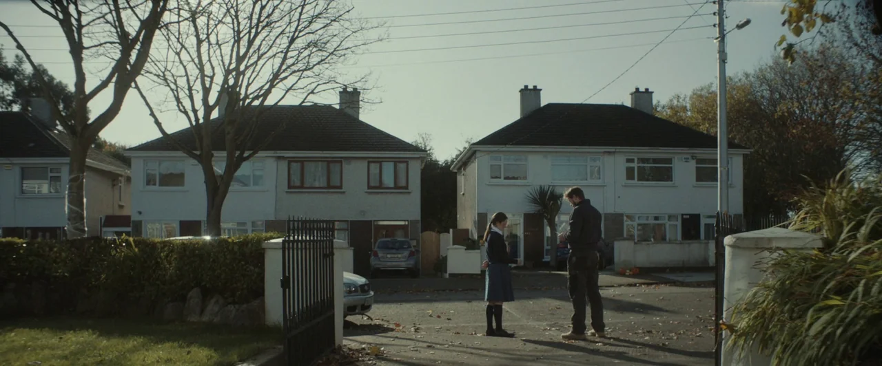 You Are Not My Mother (2021) movie still: wide — A quiet suburban street with two white two-story houses and bare leafless trees. A teenage girl and…