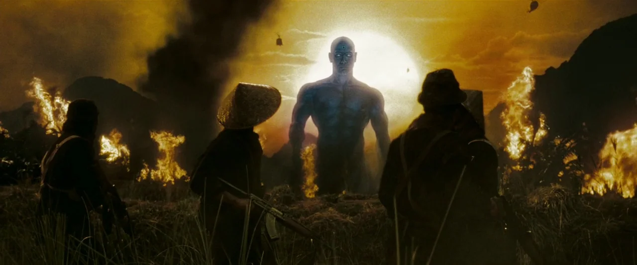 Watchmen (2009) movie still: wide — A dense, fire-ravaged jungle landscape under a bright, hazy sunset sky. Soldiers with rifles watch a towering,…