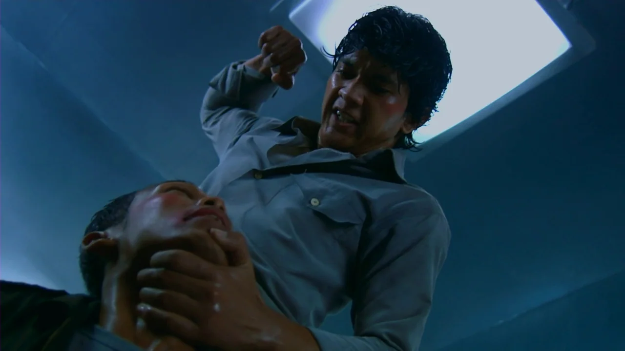 Merantau (2009) movie still: medium — A stark room features a plain wall illuminated by a single harsh overhead light. One man grips the other man's…