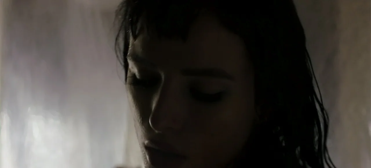 I Still See You (2018) movie still: closeup — An interior space with dim, diffuse lighting against a pale tiled wall. A woman with damp hair stands…