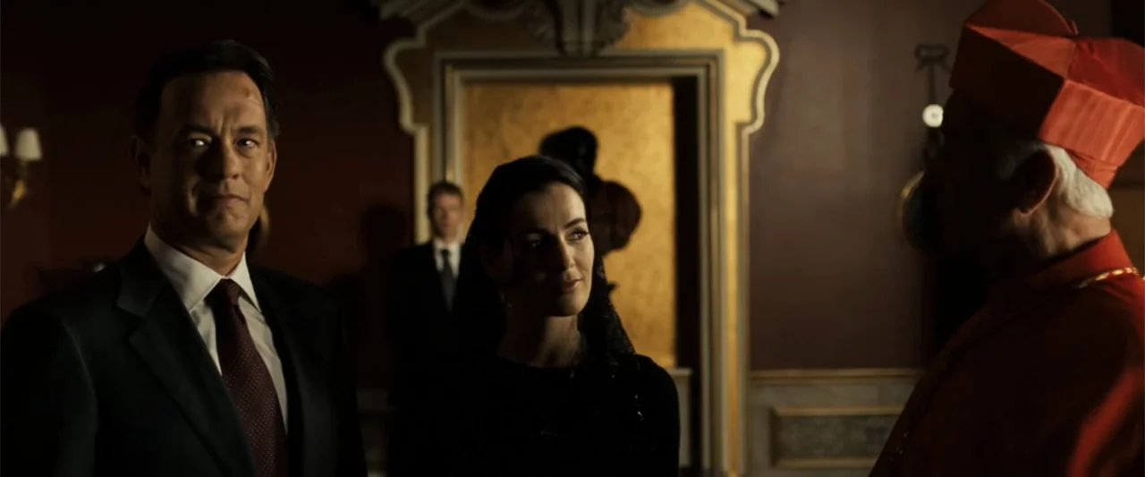 Angels & Demons (2009) movie still: medium — An ornate interior with dark red walls and gold framed doorway detail. A man and woman in formal attire…
