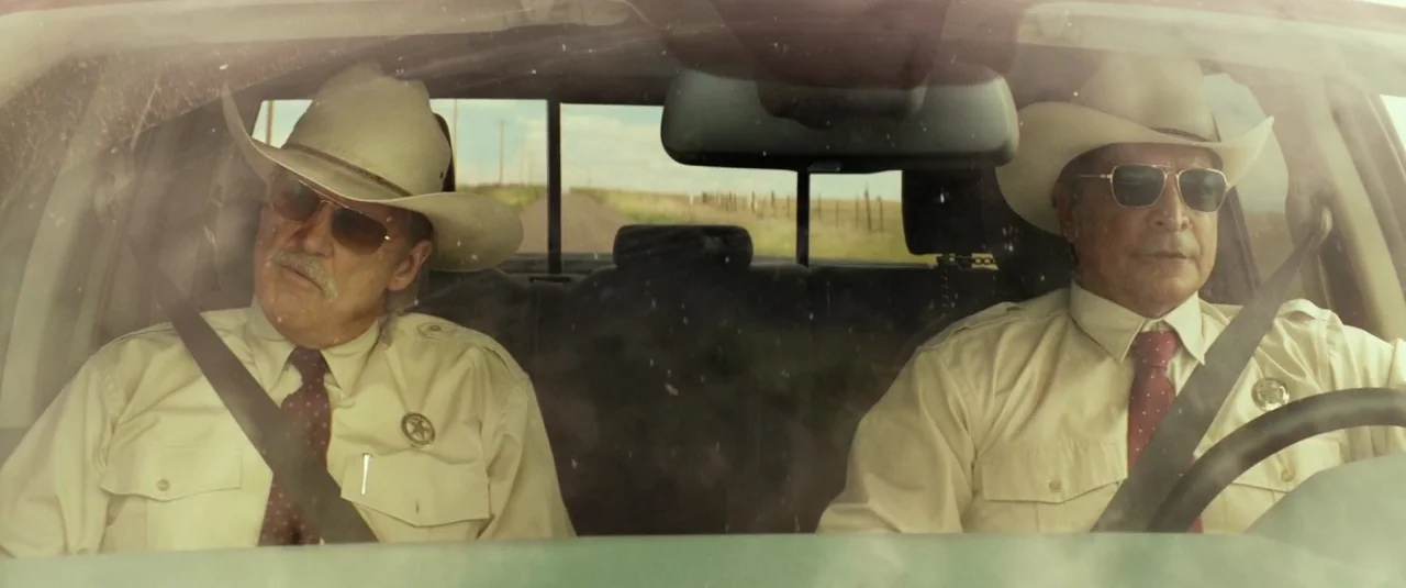 Hell or High Water (2016) movie still: medium — Two men in western-style law enforcement uniforms sit in the front seats of a vehicle. A rural dirt…