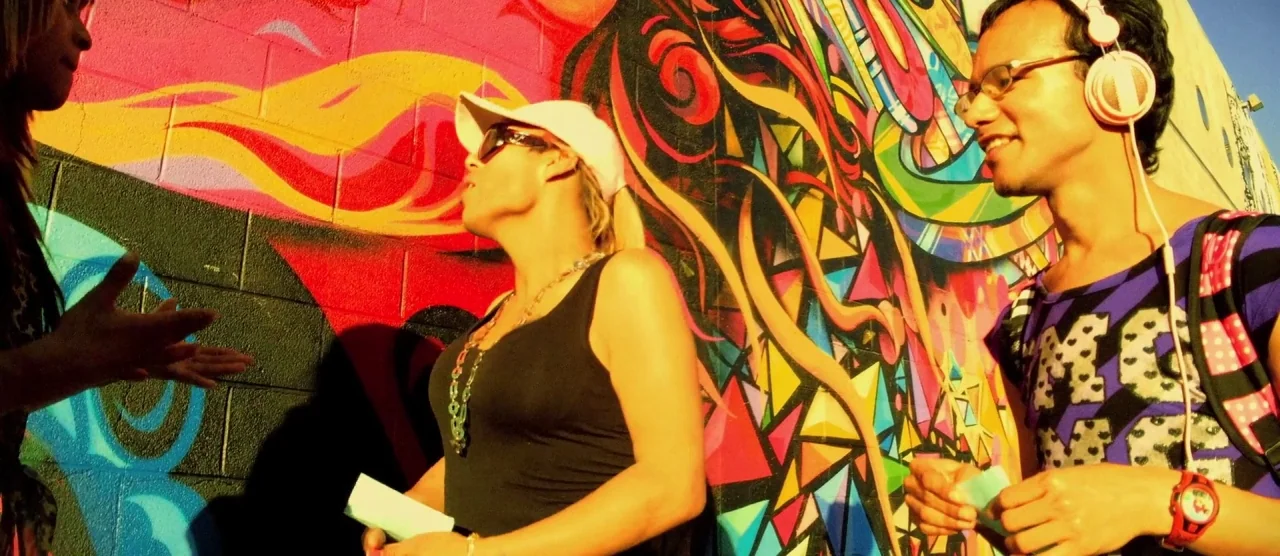 Tangerine (2015) movie still: medium — A vibrant, multi-colored abstract mural painted on a textured concrete wall during sunset. Two young people…