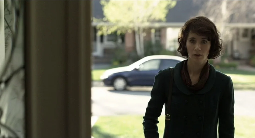 The Future (2011) movie still: medium — A suburban residential street features a blurred house and a parked sedan behind her. The woman stands…