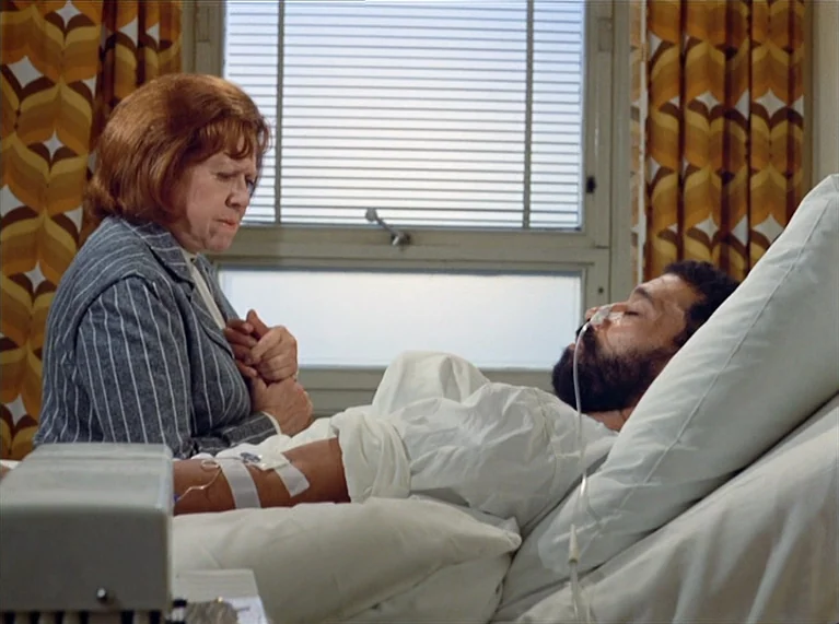 Ali: Fear Eats The Soul (1974) movie still: medium — A hospital room features patterned 1970s curtains and a window with Venetian blinds. A man lies…